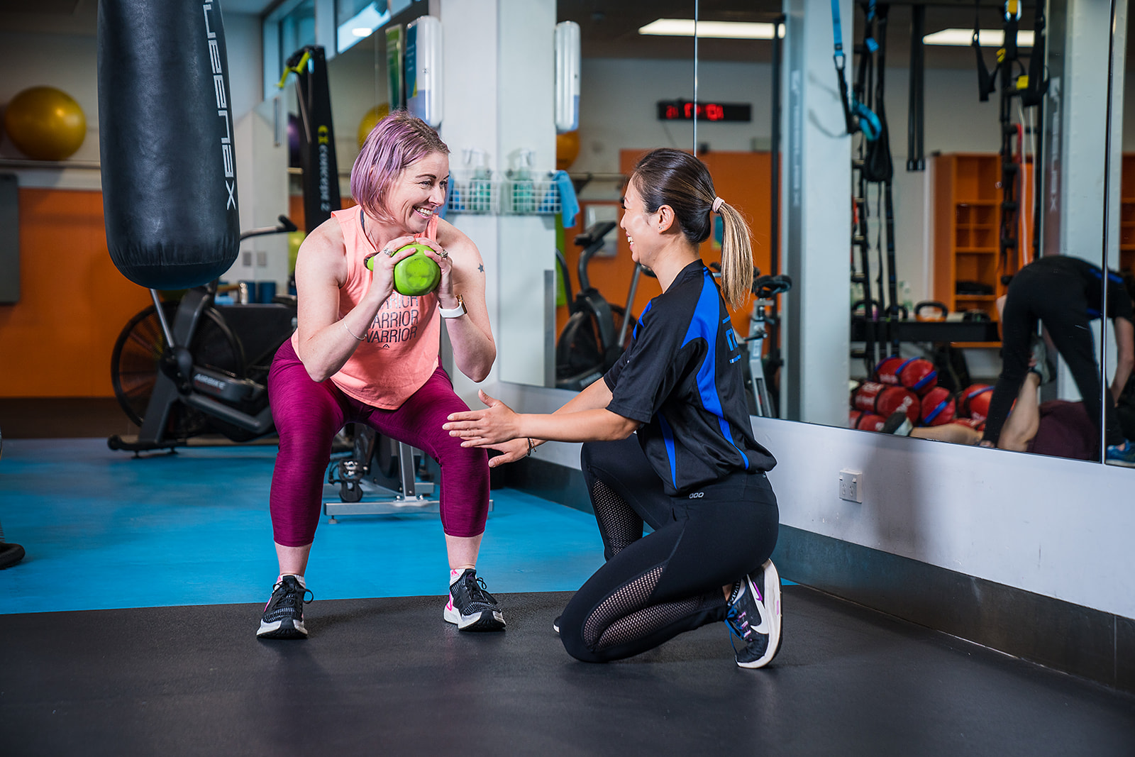 A female personal trainer assisting a woman in pink through a kettle bell workout at Christchurch Recreation and Sport Centre. 