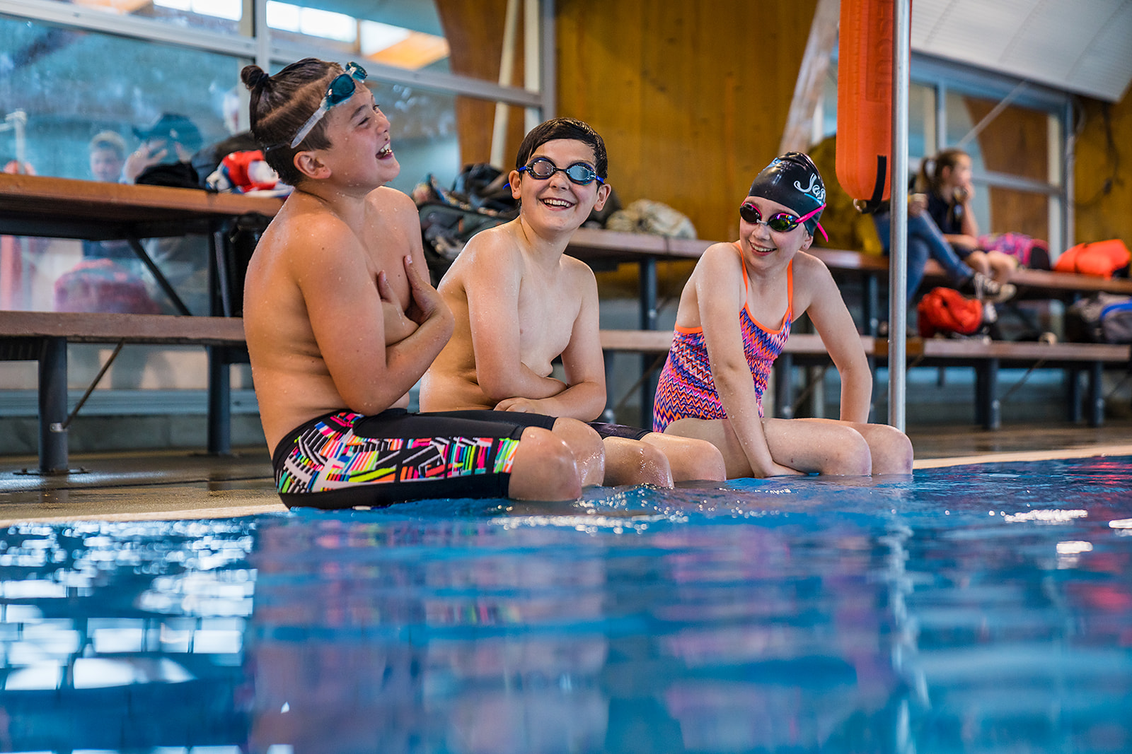 A group of smiling children sitting on the edge of the pool deck at Christchurch Recreation and Sport pool. 