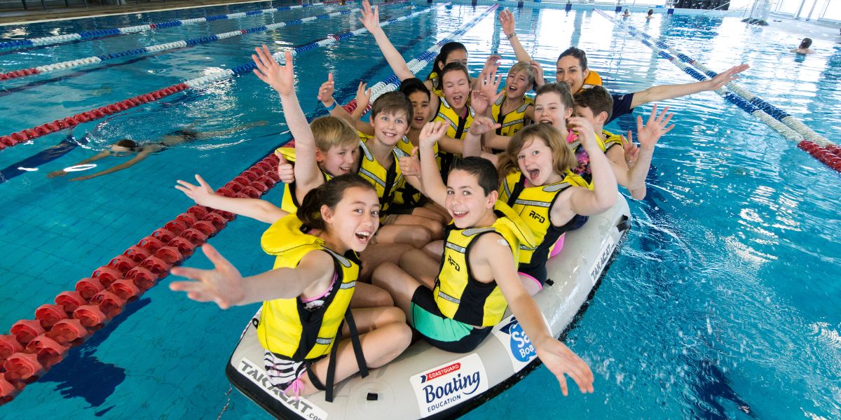A group of children in yellow life jackets sitting in a raft at Christchurch Recreation and Sport pool. 