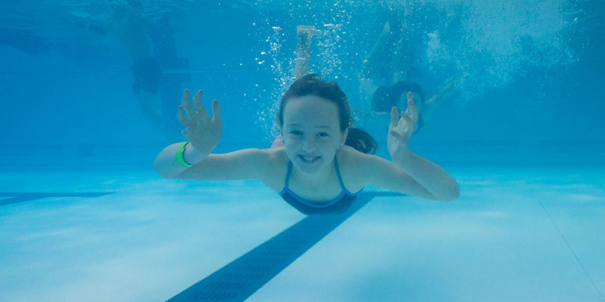 One girl under water with her eyes open, smiling shrugging her shoulders. 
