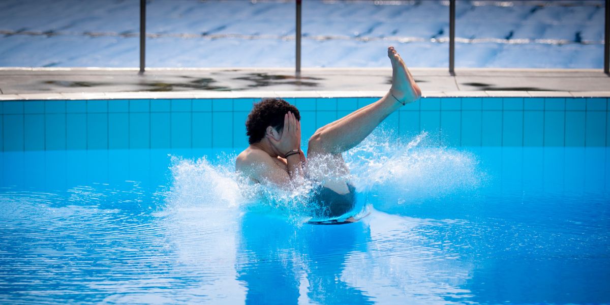 A teenage boy doing a manu off a diving board at Christchurch Recreation and Sport pool. 