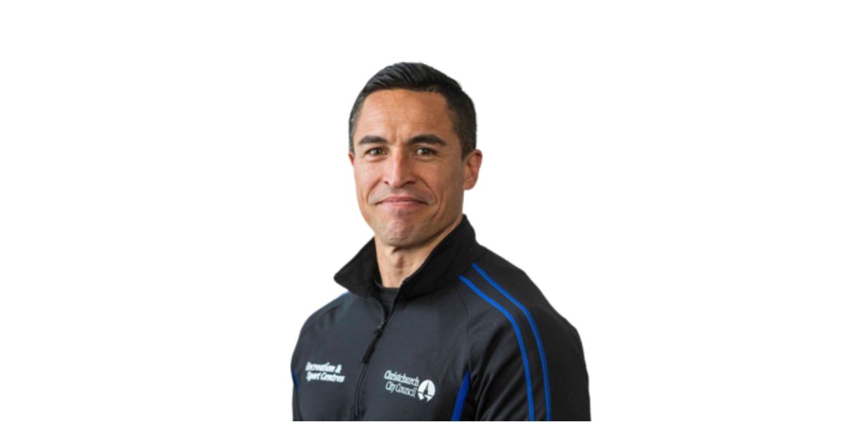 A smiling male personal trainer, Dan Hibbs, wearing a black and blue staff jacket.