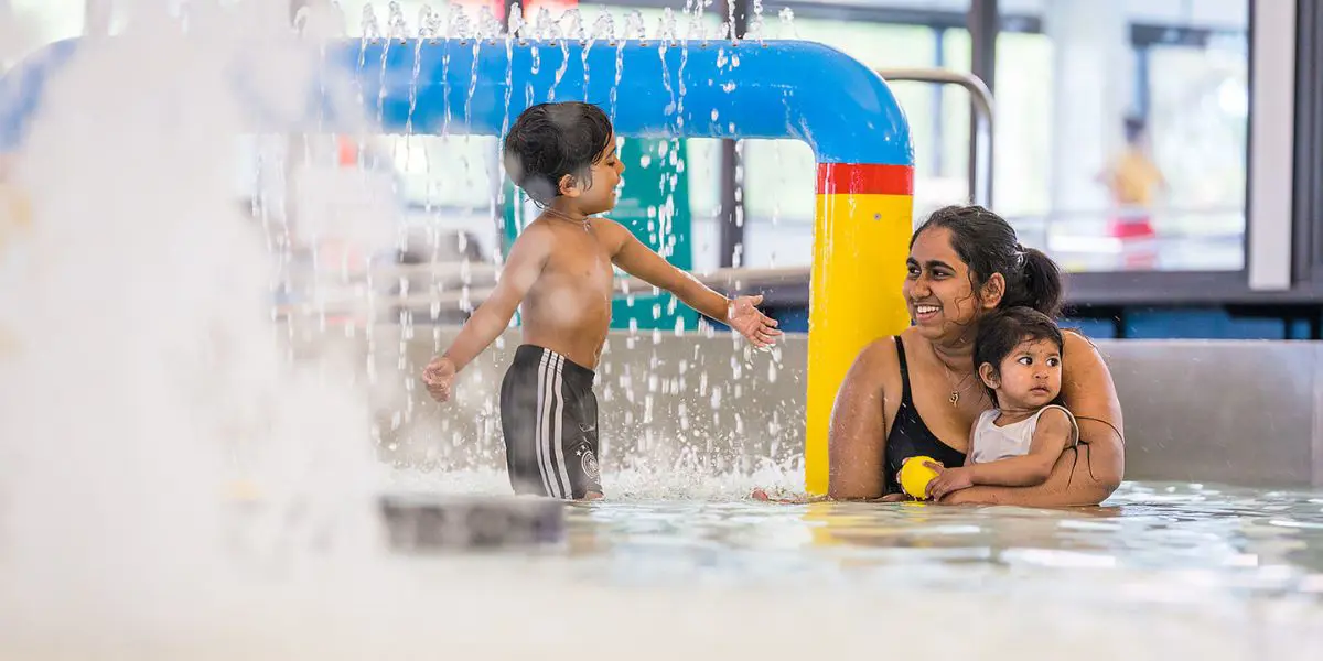 Two children playing in the toddler pool with a smiling woman at Pioneer Recreation and Sport centre.