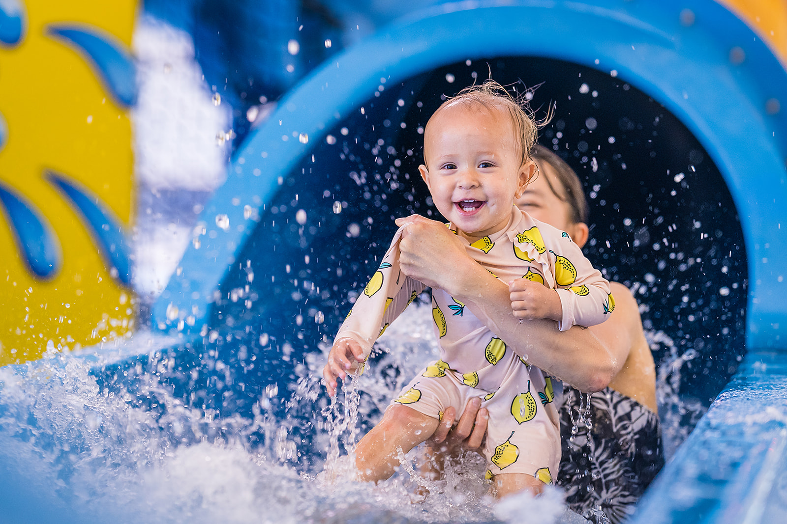 A smiling little girl being held by a woman while coming down the hydroside at Jellie Park. 