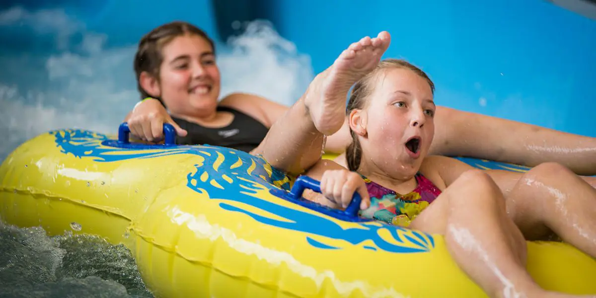 Two smiling girls sitting in a tandem yellow raft floating down the hydroslide at Christchurch Recreation and Sport pool.