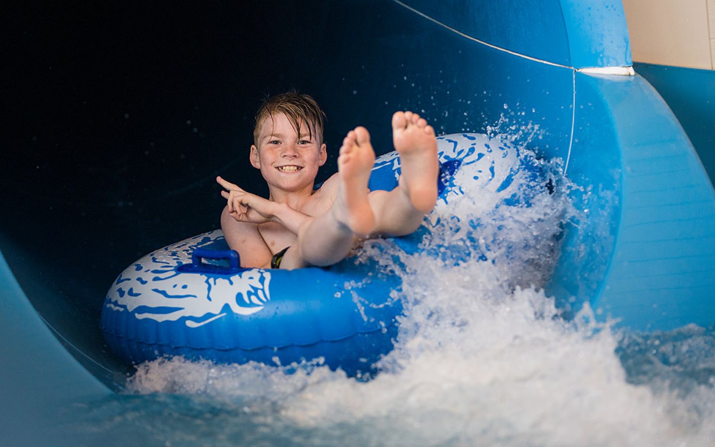 A smiling young boy on an inflatable ring coming down the hydroslide at Jellie Park Rec and Sport centre. 
