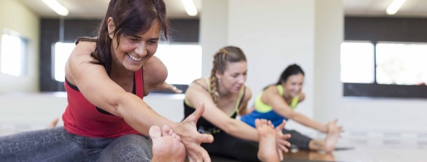 Three smiling women stretching during a yoga class at Christchurch Recreation and Sport.
